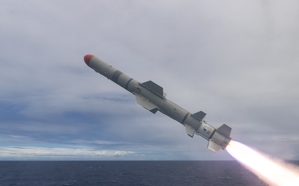 A missile is being launched from the deck of a naval warship at sea. The missile is captured mid-flight with a visible rocket exhaust plume trailing behind it. The launch appears to occur from a shipboard missile launcher system visible on the right side of the frame.