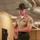 A U.S. Marine Corps Drill Instructor is photographed in what appears to be a barracks hallway. He is wearing the distinctive campaign cover (Smokey Bear hat) and khaki service uniform with visible rank insignia and service ribbons. His expression and body language suggest he is actively issuing commands or instructions.