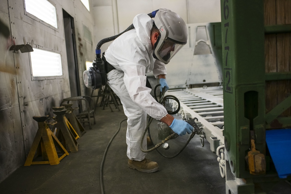 A Michigan National Guardsmen paints a Palletized Load System as a part of the corrosion prevention program