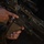 A close-up photograph of a person in US Marine Corps MARPAT digital camouflage uniform holding a Heckler &amp; Koch firearm, visible by the manufacturer markings on the lower receiver. The weapon appears to be an HK416 or similar H&amp;K assault rifle variant, equipped with a tan/FDE magazine, optical scope, and rail-mounted accessories. The image focuses on the grip area and lower receiver of the weapon.