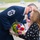 A senior U.S. Air Force enlisted member, identifiable by a Chief Master Sergeant rank insignia with command stars, presents a colorful bouquet of flowers to a woman during what appears to be an outdoor military ceremony. Both individuals are wearing face masks, consistent with COVID-19 era protocols. The setting appears to be on or near a flight line or tarmac, with other masked attendees visible in the background.