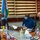 Three individuals are seated at a conference table in what appears to be an official meeting room. All three are wearing face masks, suggesting this was taken during the COVID-19 pandemic period. One individual is wearing a U.S. Navy uniform with visible 'U.S. NAVY' tape, while the others are in civilian attire, with a Djibouti flag visible in the background.