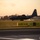 Sweden and U.S. Strengthen Air Capabilities During Swedish-led Bilateral Exercise A military turboprop aircraft, consistent with a C-130 Hercules variant, is captured landing or taking off on a runway at dusk or dawn. The warm golden-orange sky suggests sunrise or sunset conditions. Taxiway directional signage is prominently visible in the foreground.