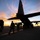 Sweden and U.S. Strengthen Air Capabilities During Swedish-led Bilateral Exercise Military personnel in camouflage uniforms are disembarking or moving alongside a large turboprop military transport aircraft on a tarmac at either sunrise or sunset. The dramatic sky features vivid orange and blue tones that silhouette both the aircraft and the soldiers. The scene appears to depict a military deployment, arrival, or training exercise at an airfield.