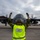 Sweden and U.S. Strengthen Air Capabilities During Swedish-led Bilateral Exercise A ground crew member from the Swedish Armed Forces is marshalling a C-130 Hercules military transport aircraft on a tarmac. The marshal is wearing a high-visibility yellow vest labeled 'Ground Handling Logistics C-130 Swedish Armed Forces' and is signaling with both hands raised. The aircraft's four turboprop engines are running, visible by the motion blur on the propellers.