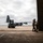 Sweden and U.S. Strengthen Air Capabilities During Swedish-led Bilateral Exercise Military personnel are observed at an airbase, standing near the open doors of a large hangar. A turboprop military transport aircraft, consistent with a C-130 Hercules variant, is parked on the tarmac outside. A forklift or ground support vehicle is positioned near the aircraft, suggesting loading or maintenance operations.