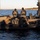 Sweden and U.S. Strengthen Maritime Capabilities During Swedish-led Bilateral Exercise The image shows a group of military or special operations personnel aboard two black rigid inflatable boats (RIBs) on a body of water. Several individuals are wearing tactical gear, plate carriers, and face coverings, suggesting a training exercise or operational activity. The setting appears to be a coastal or lake environment with a treeline visible in the background.