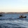 Sweden and U.S. Strengthen Air Capabilities During Swedish-led Bilateral Exercise The image shows a maritime scene with two watercraft on open water. A rigid inflatable boat (RIB) in the foreground carries several individuals in military-style uniforms, while a gray angular patrol or special operations vessel is visible in the background flying a flag. The setting appears to be a coastal or large inland waterway during late afternoon light, with a tree-lined shoreline visible in the distance.
