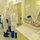 Guard medical team supports Czech partners The image shows a group of healthcare workers dressed in full personal protective equipment (PPE), including white hazmat-style suits, blue gloves, blue shoe covers, goggles, and respirator masks, standing in what appears to be a hospital isolation ward or infectious disease unit. A nursing station counter is visible on the right side, stocked with medical supplies, medications, tape rolls, and sharps disposal containers. Through a glass partition, a patient bed and an additional staff member in blue PPE are visible.