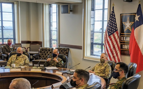A formal military meeting is taking place at a large oval conference table at U.S. Army South headquarters. Multiple military personnel in camouflage uniforms, wearing face masks, are seated around the table alongside at least one civilian. The presence of a Chilean flag and personnel wearing Chilean Army patches indicates this is a bilateral or multinational military engagement.