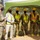 A military groundbreaking ceremony is taking place outdoors, with personnel in camouflage uniforms and high-visibility safety vests holding ceremonial gold-painted shovels. A senior military officer on the left appears to be addressing the group, which stands under a green canopy tent. All participants are wearing black face masks, suggesting this event occurred during the COVID-19 pandemic period.