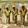 A groundbreaking ceremony is taking place outdoors under a green canopy tent, featuring five individuals holding ceremonial gold-painted shovels. Four of the participants are wearing military camouflage uniforms (OCP pattern) along with high-visibility safety vests and yellow hard hats, while one civilian wears a white hard hat with a red logo. All participants are wearing black face masks, suggesting the event occurred during the COVID-19 pandemic period.