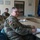 Guard medical team visits Czech Military University Hospital Prague Three U.S. Army soldiers in MultiCam/OCP camouflage uniforms are seated at a conference table in what appears to be a formal meeting room. The foreground soldier is taking notes in a binder, while two others are seated behind him. The setting includes NATO, Polish, and European Union flags, suggesting a multinational military meeting environment.
