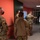 Guard medical team visits Czech Military University Hospital Prague A group of U.S. Army soldiers in OCP (Operational Camouflage Pattern) uniforms are gathered in an indoor corridor with red and green walls. They are interacting with a civilian man wearing a white mask and casual clothing, with one soldier performing an elbow bump greeting. All individuals are wearing face masks, suggesting this scene occurred during the COVID-19 pandemic period.