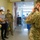 Guard medical team visits Czech Military University Hospital Prague A group of military personnel in camouflage uniforms and civilians are gathered in what appears to be a hospital corridor or medical facility. All individuals are wearing face masks, suggesting this may be during a pandemic-related visit or medical assistance mission. One soldier on the right appears to be adjusting his mask while others are engaged in conversation.