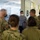 Guard medical team visits Czech Military University Hospital Prague A group of U.S. Army personnel in OCP (Operational Camouflage Pattern) uniforms are gathered in what appears to be a hospital or medical facility corridor, conversing with two civilians. All individuals are wearing face masks, suggesting this occurred during the COVID-19 pandemic period. The setting appears to be a European medical facility based on the architectural style and signage.