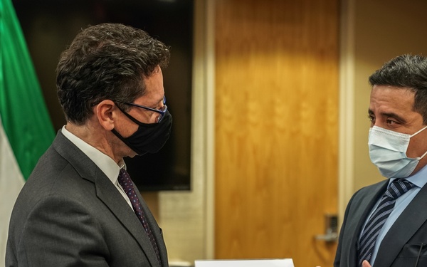 Two men in business suits wearing face masks are engaged in conversation at what appears to be an official diplomatic meeting at USAID (United States Agency for International Development). A name placard visible in the background identifies one participant as H.E. Sheikh Dr. Ahmed Nasser Al-Mohammed Al-Sabah, Minister of Foreign Affairs of the State of Kuwait. The Kuwait national flag is visible in the background, indicating a formal bilateral meeting.