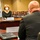 A formal meeting is taking place in a USAID conference room between officials seated at opposite sides of a table. The woman facing the camera is identified by her nameplate as Bonnie Glick, USAID Deputy Administrator, wearing a face mask. The man in the foreground, seen from behind, has a nameplate identifying him as H.E. Mikko Hautala, Ambassador of the Republic of Finland to the U.S.