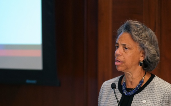 A woman is speaking at a podium during a 2022 conference focused on tuberculosis. The event appears to be a joint initiative between USAID and the National Academies of Sciences, Engineering, and Medicine. The conference banner reads 'Accelerating Progress to End TB 2022.'
