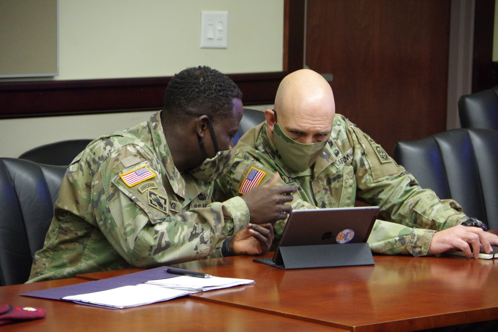 Senior enlisted leadership leaning over and talking at meeting room table during a pre-JRTC RTN 21-04 rotational brief.