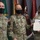 Three U.S. Army soldiers in OCP (Operational Camouflage Pattern) uniforms pose for a formal photo during an award ceremony. The soldier on the right is holding a certificate identified as the 'Sergeant Major Jerome Pionk Excellence in Retention Medal' along with what appears to be a Meritorious Service Medal citation. All three individuals are wearing black face masks, consistent with COVID-19 era protocols.
