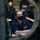 USS Ohio Operations Underway Several U.S. Navy personnel in dark blue uniforms are gathered in what appears to be a submarine control room or similar naval vessel interior. All visible individuals are wearing black face masks. The central figure, identifiable by a name/ship patch, appears to be attentively observing equipment or a briefing.