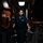 USS Ohio Missile Technician Portrait A young male service member in dark blue naval coveralls stands confidently in a narrow machinery space aboard what appears to be a U.S. Navy vessel. He is posed between heavy industrial equipment in a well-lit but confined engine or mechanical room with red-painted bulkheads. His uniform includes a name tag, rating badge, and qualification insignia consistent with U.S. Navy enlisted personnel.