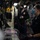 USS Ohio Operations Underway Military personnel, likely U.S. Navy sailors, are working inside what appears to be a ship's combat information center or control room. A female sailor in the foreground is seated and holding a joystick or control device, while a male sailor stands in the background. All visible personnel are wearing face masks and dark navy uniforms.