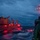 USS BARRY and JMSDF JS TOWADA Night Replenishment at Sea A nighttime or dusk replenishment-at-sea (RAS) operation between two naval vessels, with transfer lines and hoses visibly connecting them across churning water. Red navigation and work lights illuminate the scene, creating dramatic contrast against the dark blue sky and turbulent sea. The operation appears to be underway with active fluid transfer lines suspended between the ships.