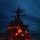 USS BARRY and JMSDF JS TOWADA Night Replenishment at Sea A naval warship, likely a U.S. Navy guided-missile destroyer, is photographed at dusk or night with crew members visible on deck and superstructure. Red and amber lighting illuminates the scene, consistent with night operations protocols where red light preserves crew night vision. Multiple personnel are gathered on the main deck and elevated platforms, suggesting an active operational evolution such as replenishment at sea or a deck evolution.