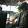 75th EAS moves cargo in East Africa Two military aircrew members are seated in the cockpit of a large military transport aircraft, likely a C-130 or similar platform. The foreground figure wears multicam/OCP camouflage, a flight helmet with night vision goggle mount, a communications headset, and a green-tinted visor. The cockpit displays numerous analog and digital instruments, multifunction displays, and overhead panel switches.