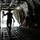 75th EAS moves cargo in East Africa The image shows the interior of a large military cargo aircraft, likely a C-17 Globemaster or C-130 Hercules, viewed from the rear cargo bay looking toward the open ramp. A silhouetted figure is walking toward the open rear ramp while carrying chains, suggesting cargo loading or unloading operations. The strong backlight from the open ramp creates a dramatic silhouette effect against the dark interior.