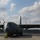 75th EAS moves cargo in East Africa A large gray military turboprop transport aircraft, consistent with a C-130J Hercules variant, is parked on a flight line apron. The aircraft is stationary with wheel chocks visible and engines not running. The setting appears to be a military air base with support structures and vehicles visible in the background.