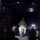 A nighttime military operation showing personnel inside what appears to be a large military transport aircraft with its rear cargo ramp open. At least one soldier in camouflage uniform is visible in motion, possibly exiting or boarding the aircraft, while another personnel appears to be directing or signaling. External lights are visible through the open ramp in the dark background.