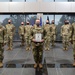 A group of approximately 12 military personnel in OCP (Operational Camouflage Pattern) uniforms are posed for a formal group photo inside a modern building. The central figure holds a commemorative plaque bearing the text 'SEMPER SUPRA' and the Space Force delta insignia. All personnel are wearing black face masks, suggesting this photo was taken during the COVID-19 pandemic period.