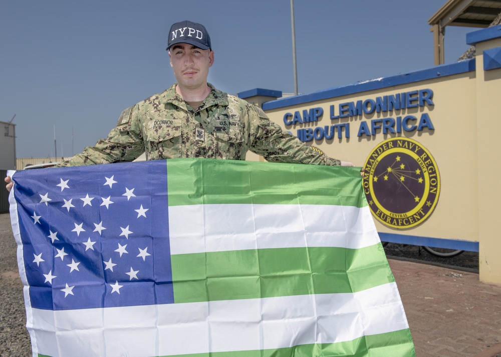 U.S. NAVY SAILOR POSES WITH AN NYPD FLAG IN DJIBOUTI
