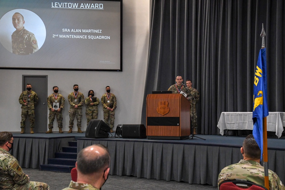 A military awards ceremony is taking place in an auditorium where the Levitow Award is being presented to SRA Alan Martinez of the 2nd Maintenance Squadron. A service member is speaking at a wooden podium on stage while several award recipients wearing medals stand in a line behind him. The event appears to be a formal Air Force recognition ceremony with an audience seated in the foreground.