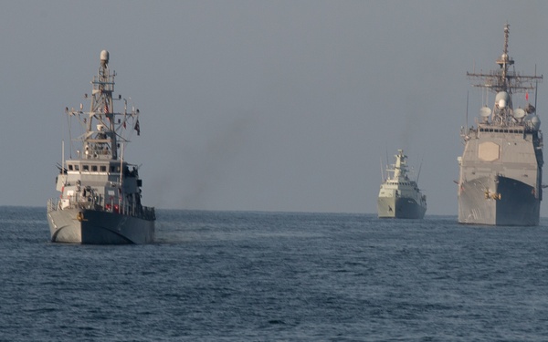 Three naval vessels are underway in formation on open ocean waters under an overcast sky. The ships appear to be military warships of varying sizes, with the largest vessel positioned on the right, a smaller patrol-type craft on the left, and a mid-sized vessel in the background center. The formation suggests a coordinated naval exercise or transit operation.