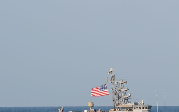 A U.S. Navy patrol coastal vessel named 'Thunderbolt' with hull number 12 is underway on open ocean waters. The ship is flying an American flag from its mast and appears to be traveling at moderate speed, generating a visible wake. The vessel is painted in standard naval gray and is equipped with various communications and weapons systems.
