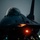 Night hot refuel of PSAB F-16 Fighting Falcons during ACE capstone event at AUAB A close-up front-facing photograph of a military fighter jet, consistent with an F-16 Fighting Falcon, taken at dusk or nighttime on what appears to be a tarmac or flight line. The aircraft's bubble canopy is prominently visible, along with orange navigation or taxi lights illuminated beneath the fuselage. The low-light conditions and dramatic lighting give the image a moody, atmospheric quality.