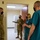 Four individuals are gathered in what appears to be a medical or military facility hallway/room entrance. Two are wearing U.S. Air Force OCP (Operational Camouflage Pattern) uniforms and two are wearing teal/green medical scrubs. All four individuals are wearing black face masks, suggesting this was taken during the COVID-19 pandemic period.