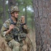 Soldier in pine forest near tree using his radio at Rotation 21-05 at the Joint Readiness Training Center