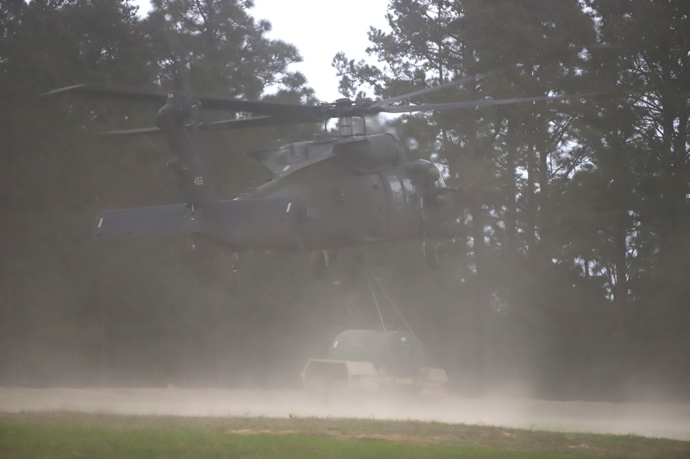 Helicopter delivers water buffalo to an open field in front of trees