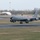 420th ABS supports Baltic Trident Exercise A U.S. Air Force KC-135 Stratotanker aircraft is captured during landing or takeoff on a runway at what appears to be a military airbase. The aircraft is painted in standard gray livery with 'U.S. AIR FORCE' markings and features a distinctive red-and-white checkered pattern on the rear fuselage. The setting appears to be a European airbase, likely in the United Kingdom, based on the surrounding landscape and infrastructure.