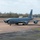 420th ABS supports Baltic Trident Exercise A U.S. Air Force KC-135 Stratotanker aerial refueling aircraft is taxiing on a military airfield apron. The aircraft is painted in overall grey livery and displays 'U.S. AIR FORCE' markings on the fuselage. The setting appears to be a European airbase, likely in the United Kingdom, based on the surrounding landscape and infrastructure.