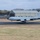 420th ABS supports Baltic Trident Exercise A U.S. Air Force aircraft, identifiable as a KC-135 Stratotanker, is captured during takeoff or landing on a runway. The aircraft bears 'U.S. AIR FORCE' markings on the fuselage and displays USAFE (United States Air Forces in Europe) insignia on the tail with the letter 'D' and serial number 80636. The background shows military airfield infrastructure including a large hangar, bare winter trees, and overcast skies.