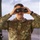 420th ABS supports Baltic Trident Exercise A U.S. Air Force service member in OCP (Operational Camouflage Pattern) uniform is looking through binoculars, apparently from inside a building with large windows. The individual holds the rank of Master Sergeant, as indicated by the chevron insignia on the chest. The setting appears to be an elevated observation post or control tower based on the large windows and outdoor visibility in the background.