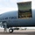 420th ABS supports Baltic Trident Exercise A U.S. Air Force aircraft, serial number 0036, is parked on a tarmac with its large cargo door open on the fuselage. Personnel are visible inside the open cargo bay, which is secured with a yellow safety barrier/gate. Ground support vehicles and at least one uniformed service member are visible on the tarmac below.