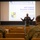 420th ABS supports Baltic Trident Exercise A military briefer wearing a face mask and flight jacket stands before an audience of uniformed personnel in a theater-style briefing room. The presentation slide behind him identifies this as a '501st Combat Support Wing - RAF Fairford Reception In-Brief' classified as UNCLASSIFIED//FOUO. The briefer, partially identified as Capt Jody Hasebe, is gesturing with both arms outstretched toward the audience.