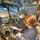 A United States Coast Guard (USCG) officer is conducting an inspection aboard a vessel's pilothouse or wheelhouse. The USCG officer, wearing a uniform with a US flag patch and 'USCG' lettering, is reviewing what appears to be a document or card while a civilian vessel operator seated at the helm reviews a form on a clipboard. Both individuals are wearing face masks, suggesting this was taken during the COVID-19 pandemic period.